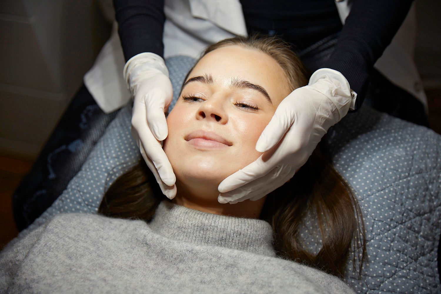 Kosmetiker med handsker undersøger kvindes ansigt før laserbehandling hos Cosmo Laser.