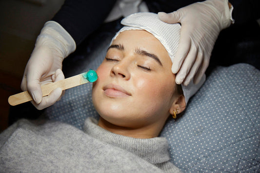 Kosmetiker hos Cosmo Laser påfører voks på en kvindes ansigt før laserbehandling.